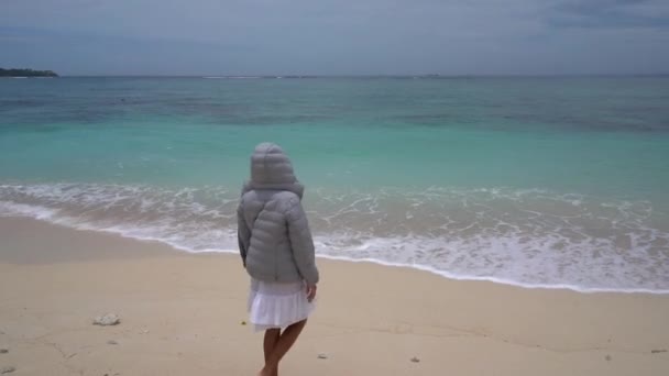 Jolie jeune femme dans une veste chaude marchant sur la plage tropicale. Mouvement lent Vidéo De Stock