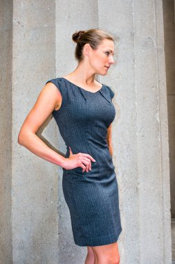 Kolsuz iş elbisesi ve dar bir topuz ile genç ve güzel bir iş kadını dışarıda duruyor ve mola veriyor.