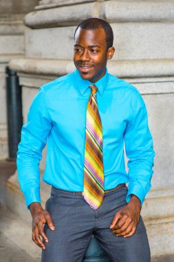 Açık mavi bir gömlek, renkli bir kravat, genç bir siyah işadamı gülümsüyor, mola vermek için dışarıda oturuyor.