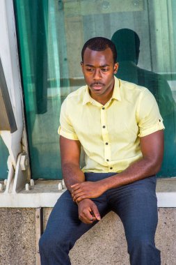 Açık sarı gömlek, gri pantolon, bilek tutan bir el, metal bir yapının yanında oturan çekici siyah bir adam, derin düşüncelere daldı.
