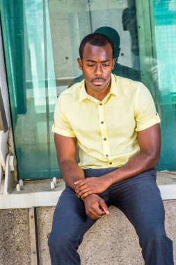 Açık sarı gömlek, gri pantolon, bilek tutan bir el, metal bir yapının yanında oturan çekici siyah bir adam, derin düşüncelere daldı.