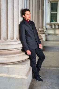 Kırmızı fanila, siyah ceket, siyah kot pantolon ve siyah kravat giyen genç ve yakışıklı bir iş adamı, ofisin dışındaki bir sütuna yaslanmış, derin düşüncelere dalıyor.