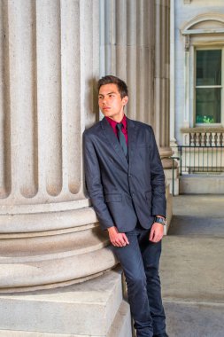 Kırmızı bir fanila, siyah bir ceket, siyah bir kot pantolon ve siyah bir kravat giyen bir üniversite öğrencisi kampüsün dışında bir köşeye yaslanıyor, rahatlıyor ve düşünüyor..