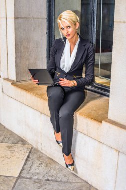 Beyaz iç çamaşırı ve siyah bir takım elbise giyen genç bir üniversite öğrencisi dışarıda bir Windo 'nun yanında dizüstü bilgisayar üzerinde çalışıyor.