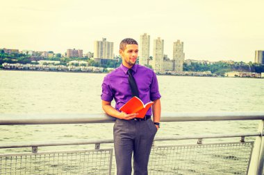 Dışarıda kitap okuyan genç adam. Mor gömlekli, gri pantolonlu, siyah kravatlı, cebine elini sokan, kaşlarını çatan, sakallı, kırmızı bir kitap okuyan genç, seksi bir adam.