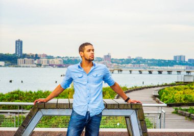 Seni Bekleyen Adam. Açık mavi gömlekli, kot pantolonlu, sakallı, bıyıklı genç bir adam nehrin kenarında seni arıyor.