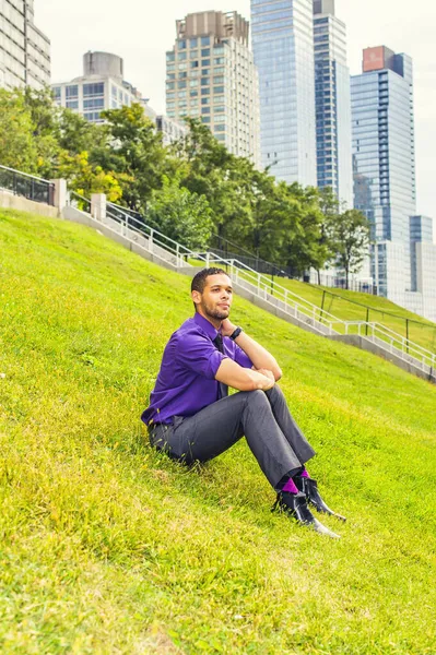 Młody Człowiek Siedzący Trawie Ubieranie Się Purpurową Koszulę Szare Spodnie — Zdjęcie stockowe