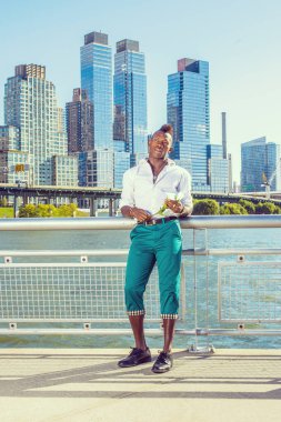 Seni özledim. Beyaz gömlekli, yeşil pantolonlu, deri ayakkabılı, Mohawk saçlı genç siyah bir adam binaların önünde beyaz bir gül tutuyor ve düşünüyor. Şehir Gelişigüzel Fashio