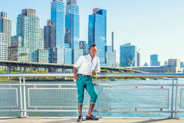 Seni özledim. Beyaz gömlekli, yeşil pantolonlu, deri ayakkabılı, Mohawk saçlı genç siyah bir adam binaların önünde beyaz bir gül tutuyor ve düşünüyor. Şehir Gelişigüzel Moda