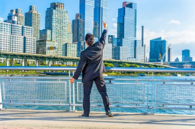 New York 'un dramatik yüksek binalarıyla karşı karşıya kalan orta yaşlı bir işadamı, başarının bir simgesi olarak elini kaldırıyor.