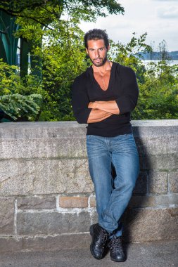 Siyah kazak, kot pantolon ve deri ayakkabılar, çapraz kollar, yakışıklı, seksi, bıyıklı ve sakallı orta yaşlı bir adam yarı duvar çitlerine yaslanmış, ciddi ciddi sana bakıyor.