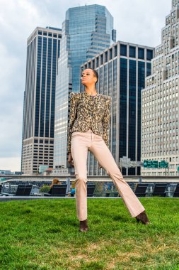 Dressing in black and yellow pattern jacket, light cream colored pants,  a young black businesswoman is standing in the front of a business district, confidently looking forward