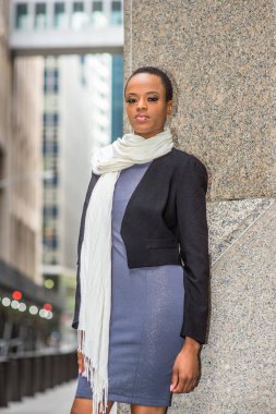 Siyah yün bir ceket, gri bir elbise, boynunda uzun beyaz bir eşarp, genç bir siyahi iş kadını ofisin dışında seni bekliyor..