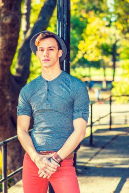 Dışarıdan Düşünen Adam. Gri uzun kollu, yuvarlak taçlı Henley gömlekli, kırmızı kotlu, yün bir Fedora şapkalı genç yakışıklı bir adam siyah bir direğe yaslanmış, yorgun, düşüncelere dalmış.