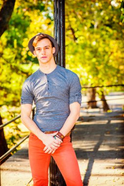 Adam dışarıda dinleniyor. Gri uzun kollu, yuvarlak taçlı Henley gömlekli, kırmızı kotlu, yün bir Fedora şapkalı genç yakışıklı bir adam siyah bir direğe yaslanmış, yorgun, düşüncelere dalmış.