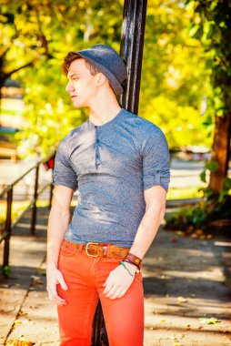 Adam dışarıda dinleniyor. Gri uzun kollu, yuvarlak taçlı Henley gömlekli, kırmızı kotlu, yün bir Fedora şapkalı genç yakışıklı bir adam siyah bir direğe yaslanmış, yorgun, düşüncelere dalmış.