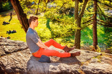 Yalnız Adam. Gri uzun kollu, yuvarlak taçlı Henley gömlekli, kırmızı kot pantolonlu, kahverengi çizmeli, yanında Fedora şapkalı genç bir adam sonbaharda kayaların üzerinde oturuyor, rahatlıyor, düşünüyor..