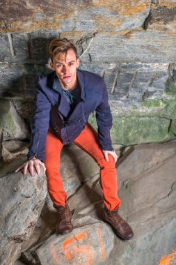 Oğlunun üzerine eğilmiş genç bir adam kayalardan bir mağarada duruyor, yukarı bakıyor ve düşünüyor.