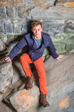 Oğlunun üzerine eğilen genç bir adam kayalardan bir mağarada duruyor, yukarı bakıyor ve tırmanıyor.