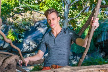 Uzun kollu, yuvarlak taçlı Henley tişörtü giyen genç yakışıklı bir adam ahşap bir alanda dikiliyor, elinde raketlerle, büyüleyici bir şekilde sana bakıyor.