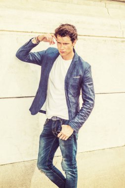 Adam günlük sokak modası. Mavi ceketli, gömleğinin altında beyaz yakalı, kot pantolonlu, kolları duvarda dinleniyor, kafaya dokunuyor, yere bakan, üzgün, düşünen genç bir adam..