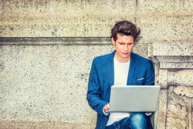 Avrupalı üniversite öğrencisi kampüsün dışında çalışıyor. Duvara yaslanmış genç bir işadamı, aşağıya bakıyor, okuyor, düşünüyor, dizüstü bilgisayarla çalışıyor. Günlük yaşamımızda teknoloji. Boşluğu Kopyala