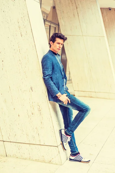 Sıradan Şehir Moda Adamı. Mavi ceketli, gömleğinin altında desenli, kot pantolonlu, şık spor ayakkabılı, genç Avrupalı bir üniversite öğrencisi ofis binasının önünde duruyor..