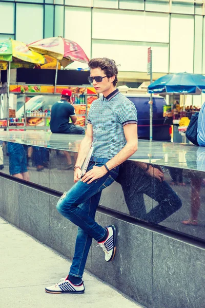 New York 'taki Avrupa Koleji öğrencisi. Kısa kollu gömlek, kot pantolon, spor ayakkabı, güneş gözlüğü, dizüstü bilgisayar tutan, sokakta mermer bir bankın karşısında duran genç bir adam,