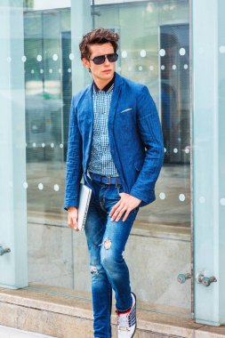 New York 'taki Avrupa Koleji öğrencisi. Mavi ceketli, kot pantolonlu, spor ayakkabılı, güneş gözlüklü, dizüstü bilgisayarlı, sokakta camdan duvara yaslanmış genç bir adam..