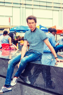New York 'ta seyahat eden Avrupalı bir öğrenci. Mavi pörsümüş kısa kollu gömlek, kot pantolon, spor ayakkabı, sokakta mermer sahnede oturan genç adam, rahatlıyor, yorgun, düşünüyor. Filtrelenmiş görünüm.