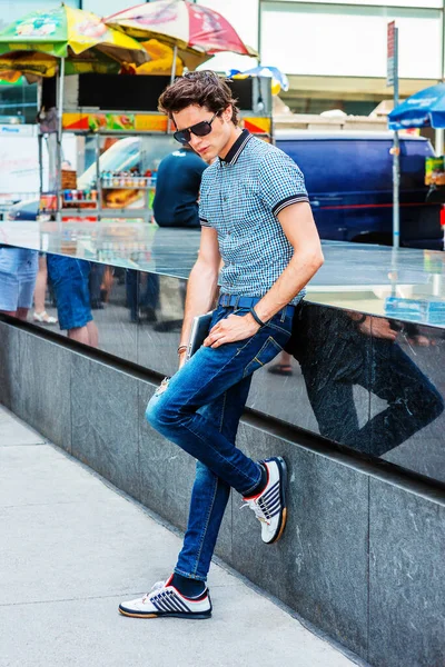 New York 'taki Avrupa Koleji öğrencisi. Kısa kollu gömlek, kot pantolon, spor ayakkabı, güneş gözlüğü, dizüstü bilgisayar tutan bir adam sokakta banka yaslanmış,.