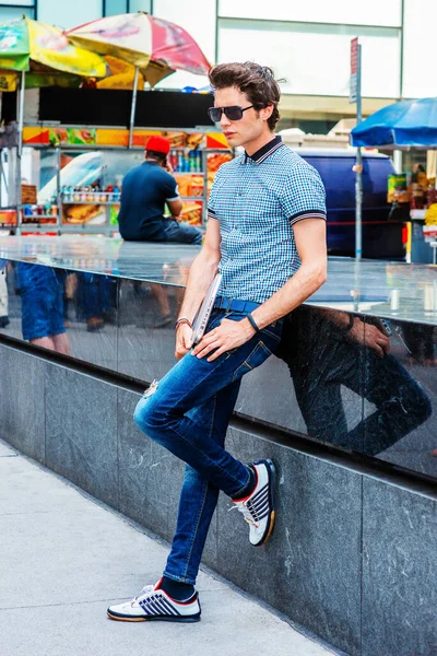 New York 'taki Avrupa Koleji öğrencisi. Kısa kollu gömlek, kot pantolon, spor ayakkabı, güneş gözlüğü, dizüstü bilgisayar tutan bir adam sokakta banka yaslanmış,.