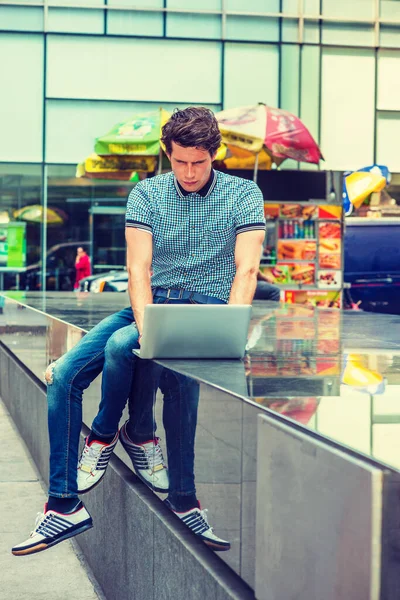 Avrupalı üniversite öğrencisi seyahat ediyor, New York 'ta okuyor. Patlak gömlekli, kot pantolonlu, spor ayakkabılı, sahnede oturan, aşağıya bakan, dizüstü bilgisayarla çalışan bir adam. Filtrelenmiş görünüm.