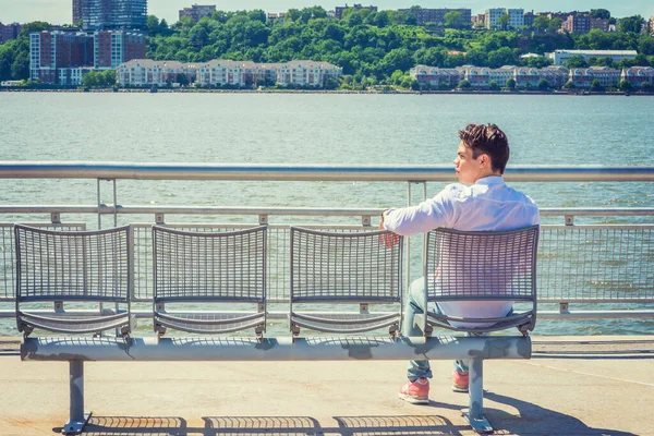 Empty Chairs for You. lonely man seeking friendship. Wearing white shirt, jeans, sneakers, a young lonely guy sitting by Hudson River in New York, facing New Jersey, waiting for you. Copy Space.