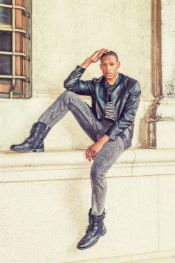 Man Urban Rastgele Moda. Siyah deri ceket, çizgili atlet, kot pantolon, deri botlar, New York 'ta duvarda oturan genç bir Afro-Amerikalı, dinleniyor, seni bekliyor.