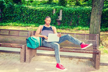 Yazın New York 'ta üniversite öğrencisi. Siyah, beyaz çizgili kolsuz bluz, kot pantolon, kırmızı spor ayakkabı çanta, kampüste sandalyede oturan, okuyan, dizüstü bilgisayarda çalışan siyah bir adam.