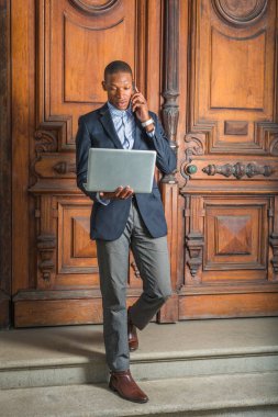 Siyah ceketli, gri pantolonlu, kahverengi deri ayakkabılı, eski tarz ofis kapısından merdivenlerden inen, dizüstü bilgisayarda okuyan, cep telefonuyla konuşan genç bir Afro-Amerikan işadamı.