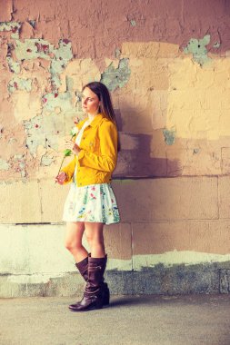 Özledim seni. Çiçek desenli iç çamaşırı giyen güzel bir kız, sarı kadife ceket, kahverengi deri yüksek çizmeler, beyaz gül tutan, duvarın yanında duran boyaları soyan, seni bekleyen