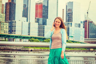 Sesini duymak güzel. Açık mavi süveter, yeşil etek, New York 'ta metal çitin yanında dikilen güzel bir Amerikalı kadın, gülümsüyor, dinliyor, cep telefonuyla konuşuyor..