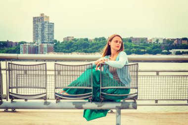 Yalnız kız seni özlüyor. Açık mavi süveter, yeşil etek, New Jersey 'in karşısında Hudson River' da metal sandalyede oturan Amerikalı bir kadın..