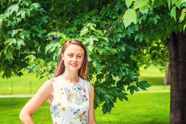 Yaz yeşili. Çiçek desenli, kolsuz, beyaz bir elbise, kampüsteki ağaçların yanında yeşil çimlerde dikilen, gülümseyen, sana bakan Amerikalı bir üniversite öğrencisi. Çevre Koruma Konsepti