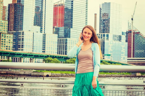 Sesini duymak güzel. Açık mavi süveter, yeşil etek, New York 'ta metal çitin yanında dikilen güzel bir Amerikalı kadın, gülümsüyor, dinliyor, cep telefonuyla konuşuyor..