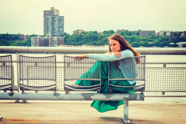 Yalnız kız seni özlüyor. Açık mavi süveter, yeşil etek, New Jersey 'in karşısında Hudson River' da metal sandalyede oturan Amerikalı bir kadın..