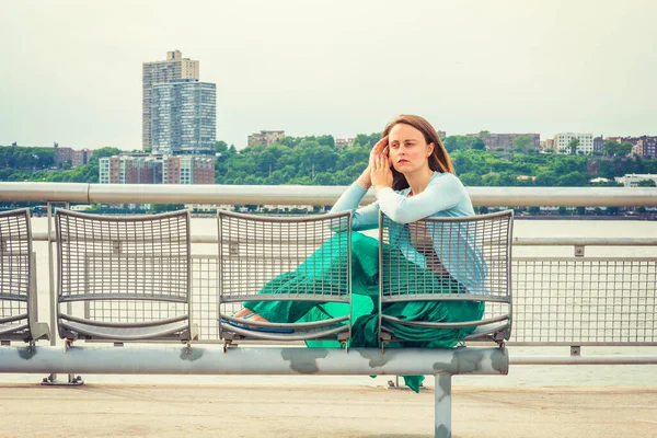 Yalnız Kız. Açık mavi süveter, yeşil etek, New Jersey 'de Hudson Nehri kıyısında metal sandalyede oturan Amerikalı bir kadın, ileriye bakıyor, ailesini, arkadaşlarını, evini özlüyor.