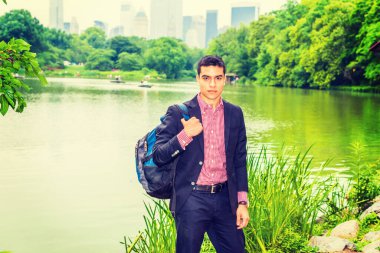 Siyah ceketli, gömleğinin altında kırmızı, beyaz desenli omuz çantası taşıyan, büyük şehirde yeşil gölün kenarında duran genç bir üniversite öğrencisi, kendine güvenen bir şekilde sana bakıyor. Çevre Koruma Konsepti