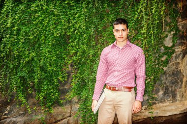 Aşk yeşili. Kırmızı desenli gömlek, sarı pantolon, dizüstü bilgisayar, duvarda uzun yeşil yapraklarla duran genç bir öğrenci, sana bakıyor. Çevre Koruma Konsepti.