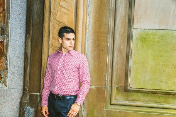 Üniversite öğrencisinin portresi. Sıradan erkek modası. Kırmızı desenli, uzun kollu gömlekli, siyah pantolonlu, klasik tarz duvara karşı duran, kendinden emin bir şekilde ileriye bakan genç bir adam. Boşluğu kopyala