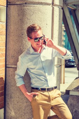 Sesini duymak güzel. Beyaz gömlek giyiyor, sarı pantolon giyiyor, güneş gözlüğü takıyor, New York 'ta güneş ışığı altında sütuna karşı duran genç bir adam, gülümsüyor, cep telefonuyla konuşuyor.