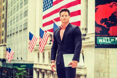 Gururlu Amerikalı İşadamı 4 Temmuz Bağımsızlık Günü, New York 'ta. Siyah takım elbiseli, dizüstü bilgisayarı olan, genç, güçlü, seksi bir adam Wall Street 'te duruyor. Arka planda Amerikan bayrakları