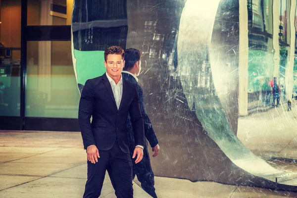 Başarılı Amerikalı İş Adamının Portresi. Siyah takım elbiseli, genç, güçlü, seksi bir adam metal ayna duvarının yanında duruyor, gülümsüyor, kendinden emin bir şekilde ileriye bakıyor..